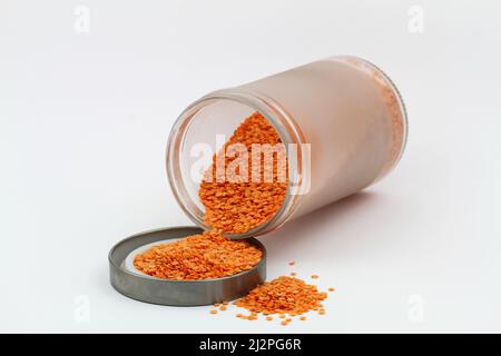 Uncooked red lentils scattered out of the glass jar on white surface Stock Photo