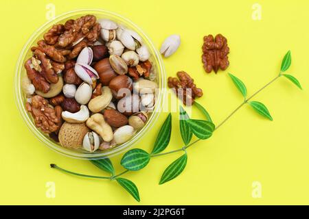 Selection of walnuts, hazelnuts, cashew nuts and almonds in plastic box on vivid yellow background Stock Photo