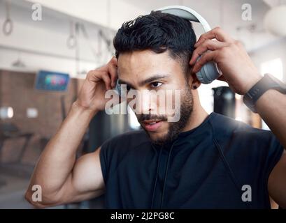 Music on, now lets begin. Shot of a sporty young man listening to music while exercising in a gym. Stock Photo