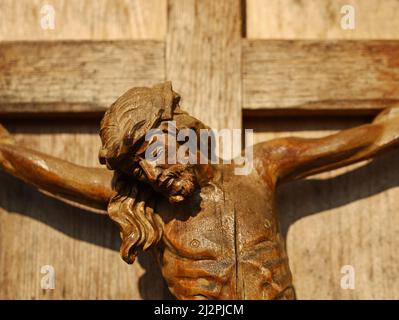 Close up of an old wooden crucifix, face of Jesus Christ on wooden cross in sunlight Stock Photo