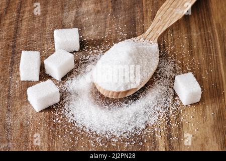 Granulated sugar in wooden spoon and sugar cubes on wooden background. Stock Photo