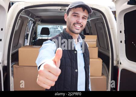 Quality service is my promise to you. Portrait of a young delivery man showing thumbs up while loading boxes from a van. Stock Photo