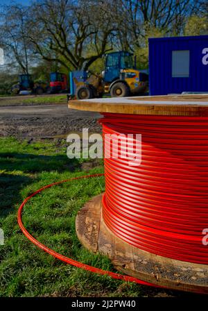 Huge cable drum of red optical fibre cable at a construction site with site vehicles and a blue  in the background Stock Photo