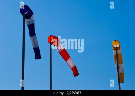 Three windsocks in blue, red and yellow with white stripes in clear blue sky Stock Photo