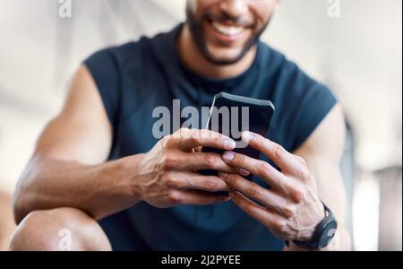 Download the best workout apps today. Low angle shot of an unrecognisable man using a cellphone in a gym. Stock Photo