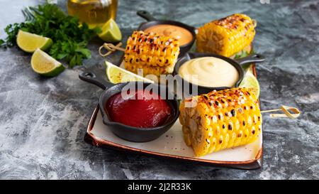 grilled cob corn with spices lime white yellow red sauce close up Stock Photo