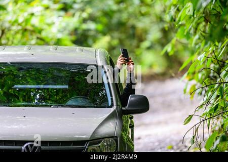 A man taking a cell phone picture from his car window. Colombia, South America. Stock Photo