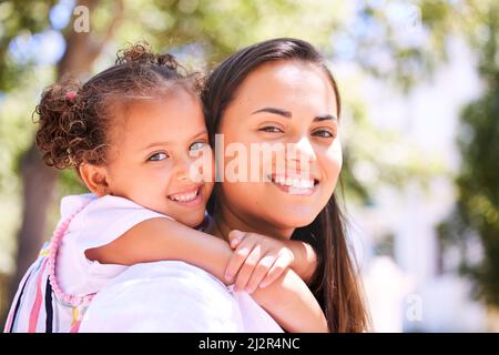 Lets go play mom. Shot of a mother giving her daughter a piggyback ride in the park. Stock Photo