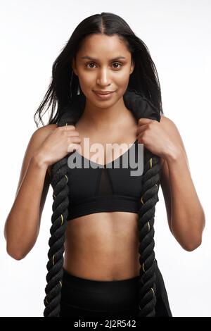 Do it for crop tops and jaw drops. Studio portrait of a sporty young woman posing with battle ropes around her neck against a white background. Stock Photo