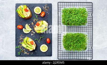 How to use microgreens in home cooking. Snacks with microgreens, avocado and tomatoes on a black slate serving tray top view. Growing vitamin microgre Stock Photo