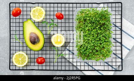 Microgreens in a tray close-up top view. Ingredients for cooking a fast and healthy snack on a baking rack. Avocado, lemon, tomato, microgreens of aru Stock Photo