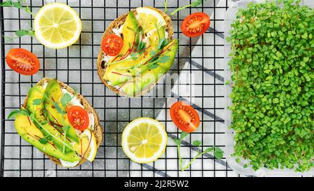 Close-up microgreen snack for healthy breakfasts at home. Ciabatta with avocado and cream cheese with microgreens on a baking rack. Growing microgreen Stock Photo