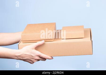 Stack of cardboard boxes in female hands. Blank brown parcel boxes on light blue background. Packaging, shopping, free shipping, delivery concept Stock Photo