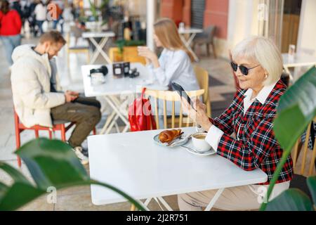 Senior woman using cellphone while having lunch in cafe Stock Photo