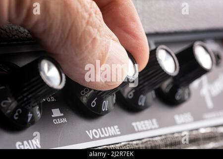 hand turning up the volume of a guitar amplifier, treble and bass control knobs out of focus , equalization dials close up, horizontal Stock Photo