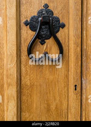 Black painted heart shaped wrought iron door knocker on wooden door painted with light brown fake wood grain effect. Stock Photo