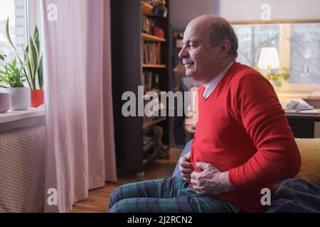 unhappy senior man suffering from stomach ache sitting at home Stock Photo