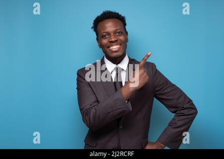 Smiling african man wearing suit looking at camera pointing aside giving advice. Portrait of black confident man at home. Successful entrepreneur feel Stock Photo