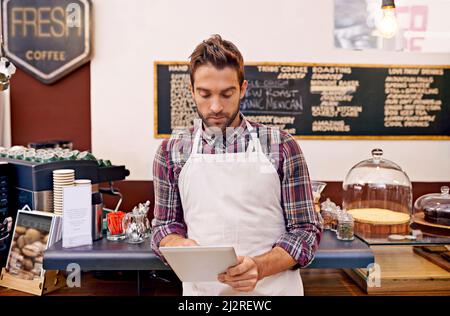 Checking out the newest coffee trends. Shot of a young barista using a digital tablet in a cafe. Stock Photo