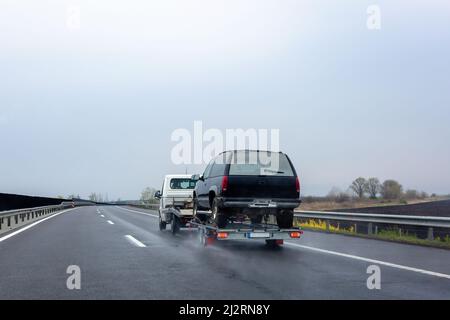 Car carrier trailer with car on wet road. Spray from under the wheels of car. Stock Photo