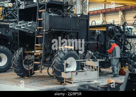 Worker assembles agricultural vehicle combine harvester in industrial factory workshop. Stock Photo
