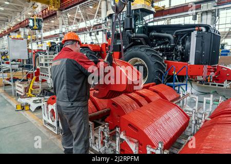Industrial worker assembles agricultural equipment in tractor or combine harvester production line in factory. Stock Photo