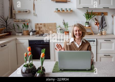 Cheerful senior woman checking information on laptop online, video call to children or friends, busy working at computer. Senior people and technology Stock Photo