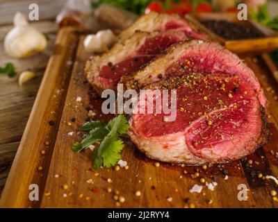 Appetizing juicy raw beef steaks with spices and parsley on a cutting board. There are no people in the photo. Recipes for restaurant and home cooking Stock Photo