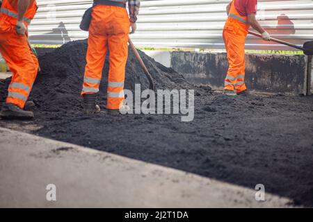 A bunch of asphalt. Workers repair the road. People in orange clothes. Asphalt pavement. Men work with shovels. Stock Photo