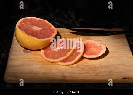 GRAPEFRUIT CUT ON LIGHT WOOD BOARD. BLACK MARBLE COUNTERTOP. Stock Photo