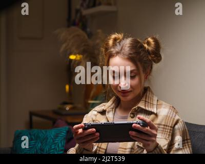 A cute girl with a portable game console plays a video game. Mobile games, modern technologies, cyberspace, virtual reality, entertainment, communicat Stock Photo