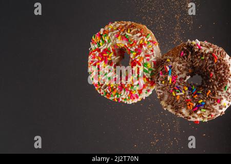 Two sweet donuts decorated with multi-colored confectionery sprinkles on a gray background. Sweet food, breakfast for two, birthday, romantic date. Th Stock Photo