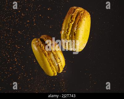 Creative composition. Two yellow French macaroons in frozen flight on a black background with chocolate dust. Restaurant, cafe, hotel, bakery. Adverti Stock Photo