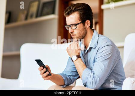 Maybe its time to switch to a new network.... Shot of a handsome young man looking confused while using a cellphone at home. Stock Photo