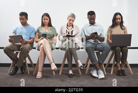 Staying focused as they each prepare for something big. Shot of a group of businesspeople using digital devices while sitting together in a line Stock Photo