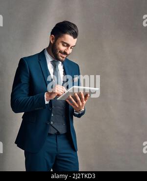Tapped into the latest corporate trends. Studio shot of a stylishly dressed young businessman using a digital tablet against a grey background. Stock Photo