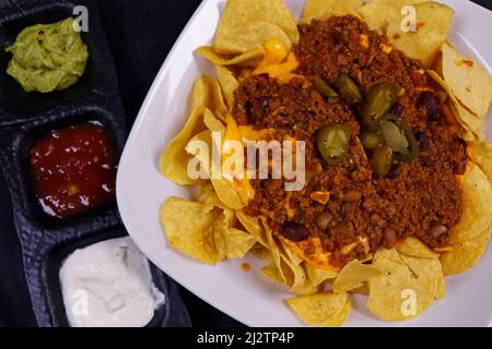 traditional mexican snack food, corn tortilla chips and avocado guacamole, chili con carne, salsa and sour cream. known as nachos Stock Photo