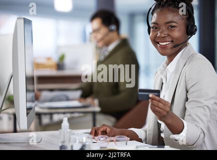 What should we buy today. Shot of a young female call center agent holding a credit card at work. Stock Photo