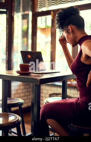 Struggling to get through her agony. Cropped shot of a young woman experiencing discomfort while working on her laptop in a cafe. Stock Photo