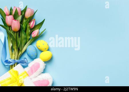 Easter composition bouquet tulips spring flowers eggs gift rabbit ears on blue background copy space Stock Photo
