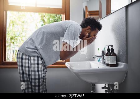 Freshening up. Cropped shot of a handsome young man washing his face in the bathroom at home. Stock Photo