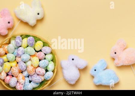 Easter composition of eggs in a basket of toy rabbits on a yellow background with a place for text. Stock Photo
