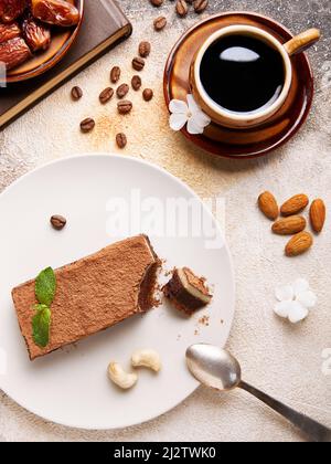 Black coffee in brown small cup, book and Healthy Sugar free Homemade Raw vegan Tiramisu cake with cashew nuts, dates inside, decorated with mint leav Stock Photo