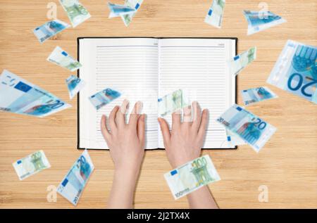 Female's hands lies on an empty book, euro banknotes are pouring down from above. Flat lay. The concept of the financial crisis and the economy. Stock Photo