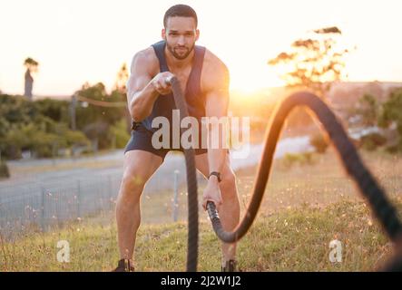 Work those muscles. Shot of a sporty young man doing heavy rope training outside. Stock Photo