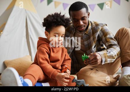 Portrait of cute toddler boy with young African American father playing together on floor in cozy kids room Stock Photo