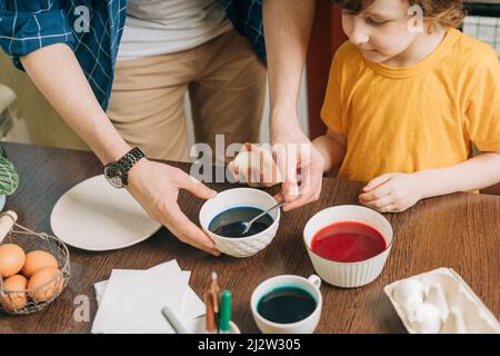 Easter day. Male Father and son painting eggs on wooden background. Family sitting in a kitchen. Preparing for Easter, creative homemade decoration Stock Photo