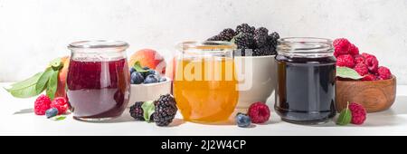 Assortment of summer seasonal berry and fruits jams in small jars, homemade preserving concept, marmalades or confitures with fresh berries on white b Stock Photo