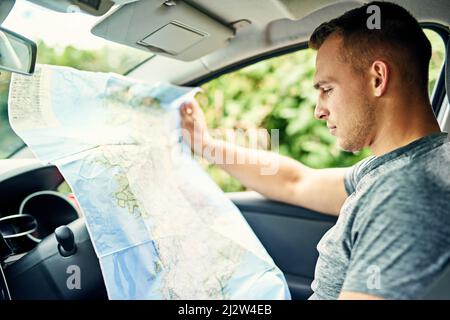 Where am I. Shot of a young man reading a map while traveling in a car. Stock Photo