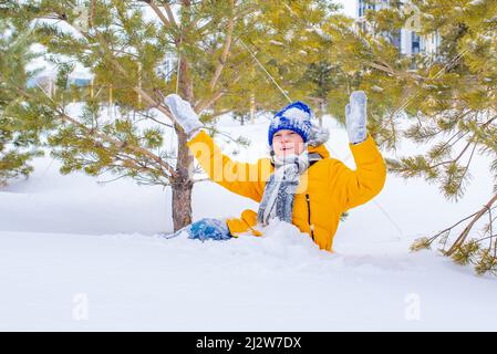 in a bright yellow jacket and a blue hat, a boy in the snow Stock Photo